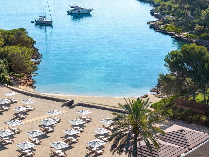 Widok na zatokę z łodziami, leżakami i palmami wzdłuż wybrzeża.