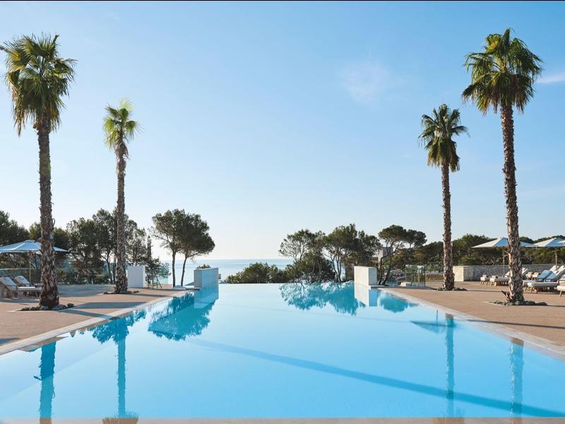 Długi niebieski basen z palmami i leżakami pod czystym niebem w ośrodku.