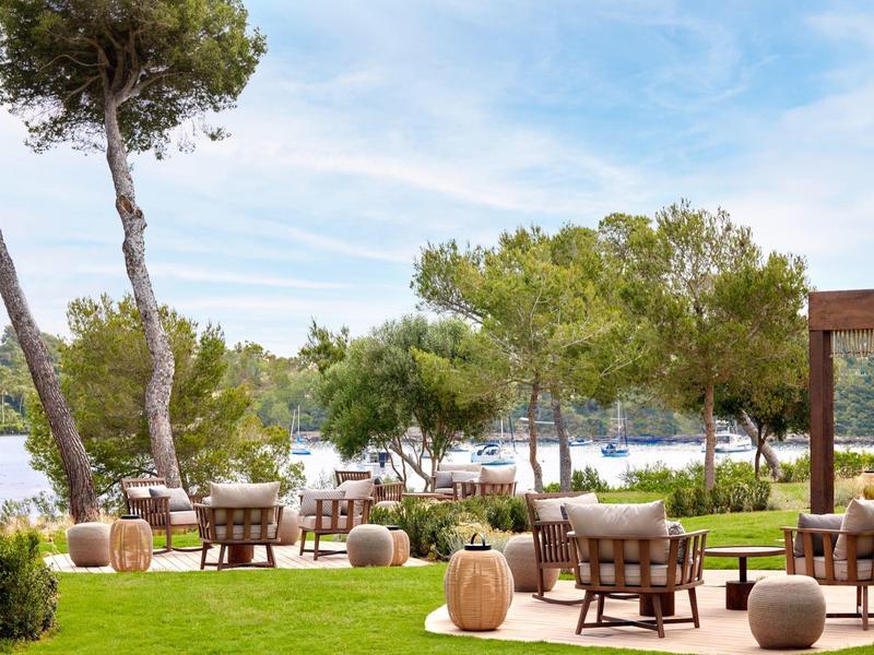 Zewnętrzny obszar hotelu z miejscami do siedzenia, stolikami i widokiem na morze przy czystym niebie.