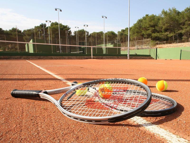 Dwie rakiety tenisowe i trzy piłki tenisowe leżą na korcie z czerwonej cegły.