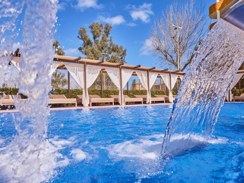 View of a pool with bubbling water and white curtains in a sunny setting.