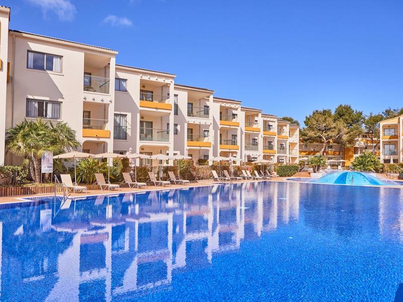 Hotel complex with large swimming pools and multi-story buildings under clear skies.