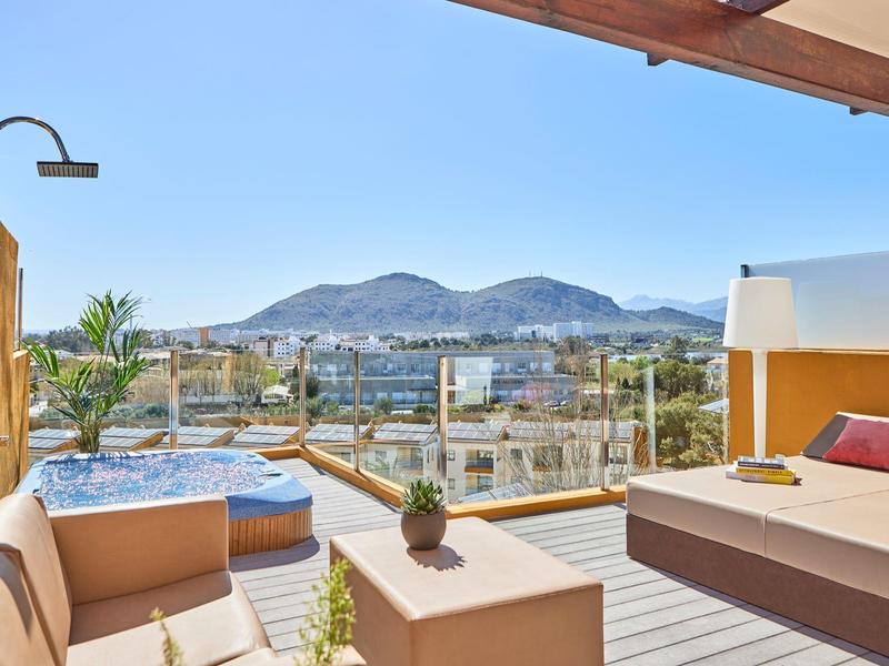 Modern balcony with hot tub, seating area, and mountain view under clear sky.