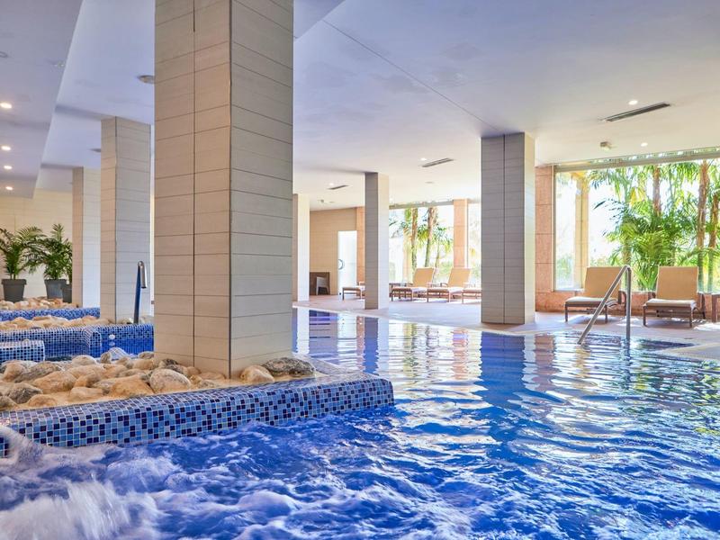 Indoor pool with whirlpool area in a bright, modern hotel featuring plants and seating areas.