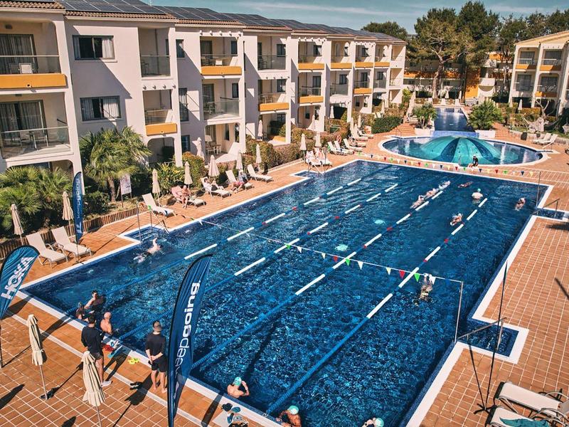 Large outdoor pool with swimming lanes, surrounded by lounge chairs and multi-story hotel buildings.