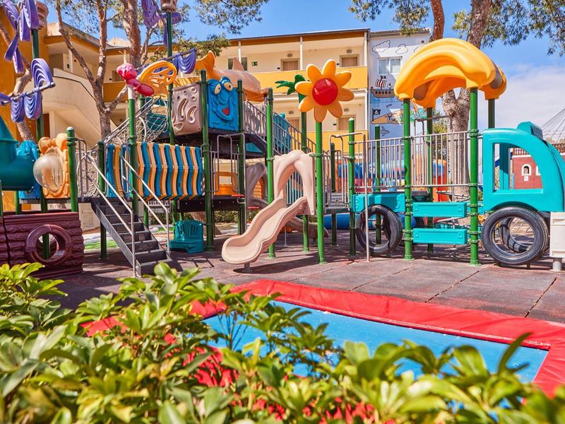 Colorful children's playground with slide and climbing frame near hotel building.