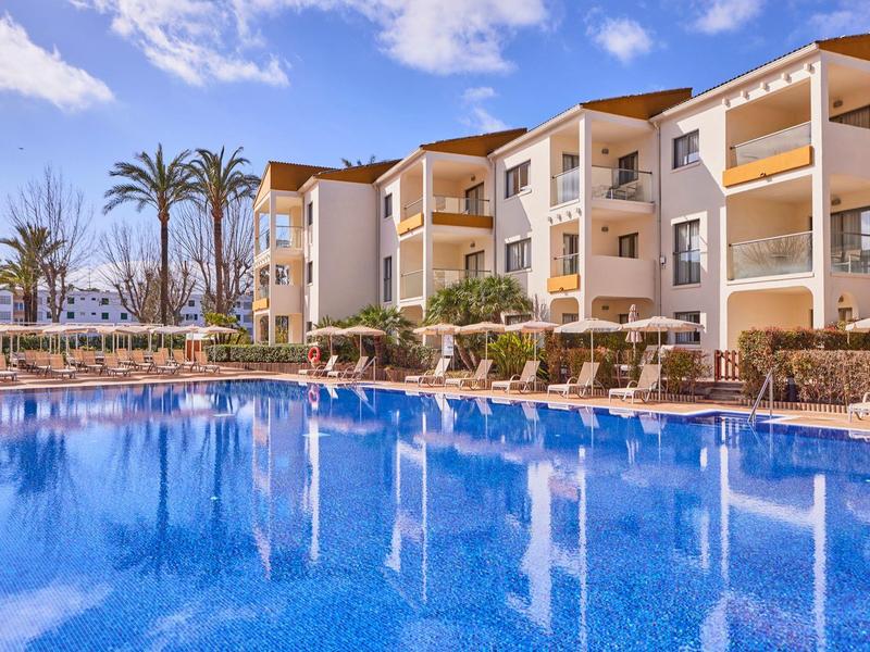 Hotel with outdoor pool, sun loungers, and palm trees under a blue sky