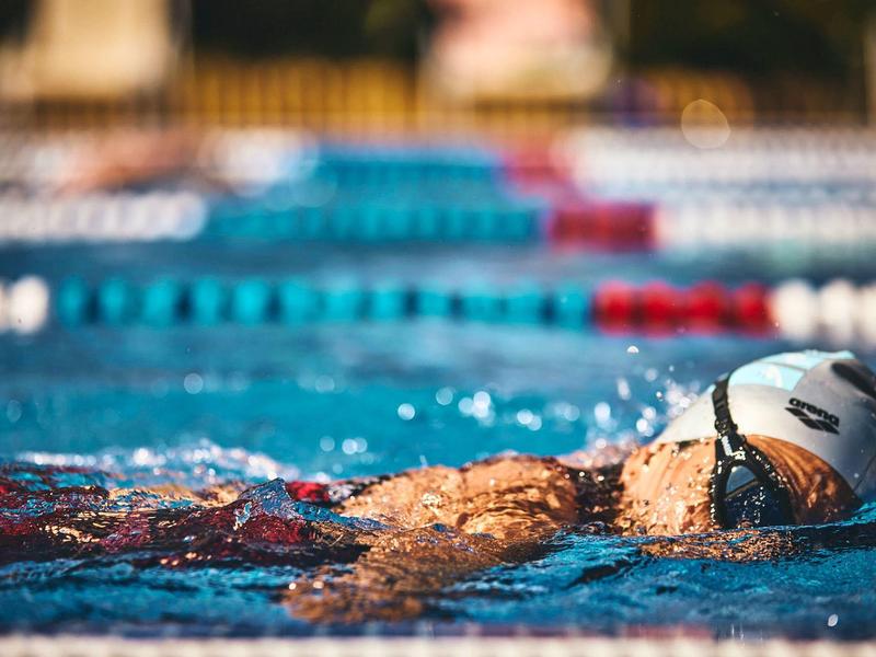 Swimmer with white swim cap swimming in a lane in an outdoor pool.
