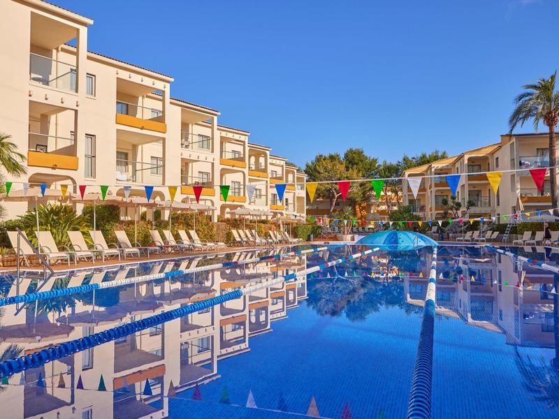 Large hotel pool with lounge chairs, colorful flags, and clear blue sky.