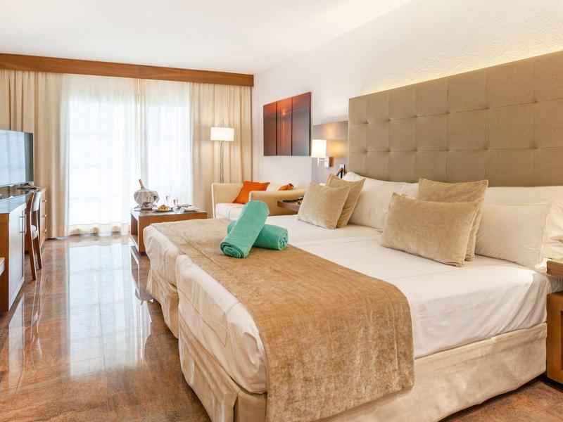 Chambre d'hôtel lumineuse avec grand lit, sol en bois et balcon donnant sur l'extérieur.