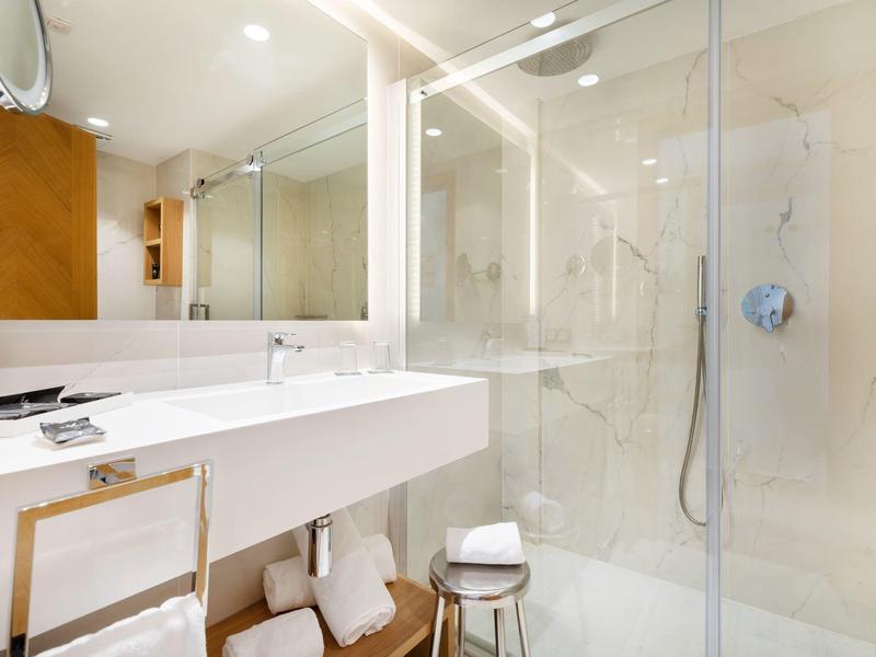 Salle de bain d'hôtel moderne avec lavabo, miroir et douche en verre à l'italienne.