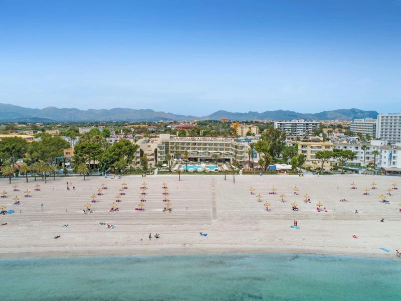 Large plage calme avec parasols et hôtels en arrière-plan à côté d'une eau bleue claire.