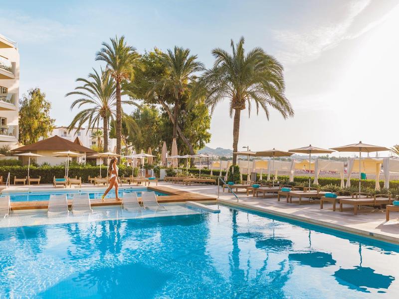 Piscine d'hôtel avec chaises longues, parasols et palmiers au coucher du soleil.