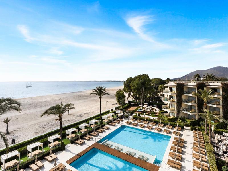Hôtel avec piscine et chaises longues sur la plage avec palmiers et vue sur la mer sous un ciel dégagé