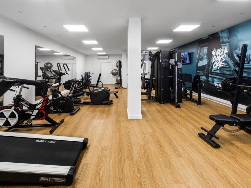Salle de sport moderne avec sol en bois, équipement cardio et musculation dans un espace lumineux