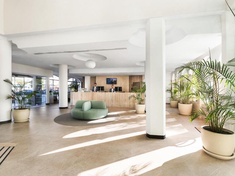 Lobby d'hôtel lumineuse avec mobilier moderne et grandes plantes en pot.