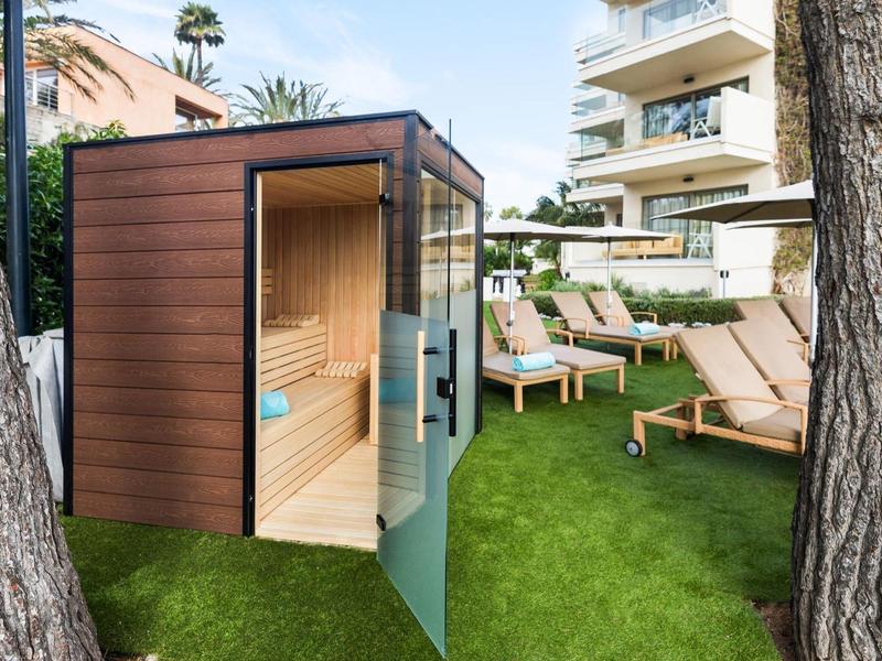 Petite cabine de sauna en bois avec porte vitrée dans le jardin d'un hôtel avec chaises longues.
