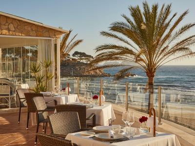 Terraza con mesas puestas, palmeras y vista al mar al atardecer.