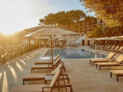 Zona de piscina del hotel con tumbonas y sombrillas al atardecer.