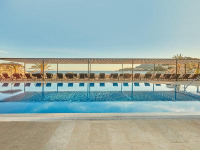 Piscine calme avec reflets, entourée de transats sous un auvent par une journée ensoleillée.