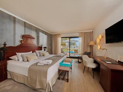 Chambre d'hôtel moderne avec lit double, bureau, chaise, télévision et balcon avec sièges extérieurs.