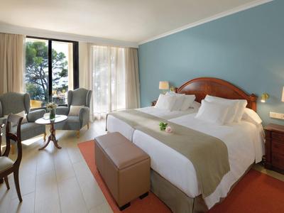 Chambre d'hôtel confortable avec grand lit, mur bleu, bureau et balcon vue sur les arbres.