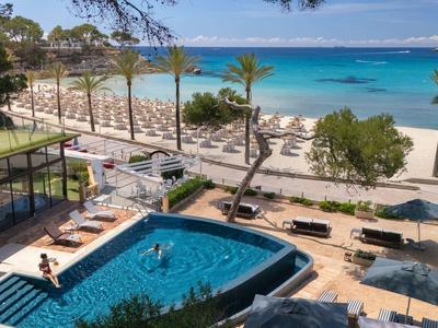 Station avec piscine, palmiers et transats surplombant une plage bleue claire.