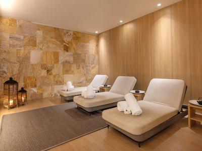 Salle de spa relaxante avec trois chaises longues, serviettes, murs en pierre et bois, éclairage chaleureux.