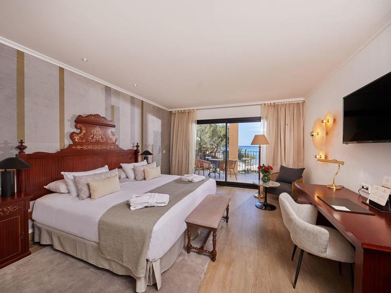 Chambre d'hôtel élégante avec grand lit, bureau en bois, chaise, TV et balcon.