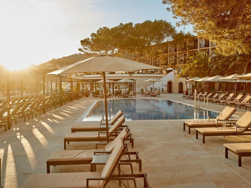 Coucher de soleil près de la piscine avec chaises longues et parasols dans un complexe hôtelier.