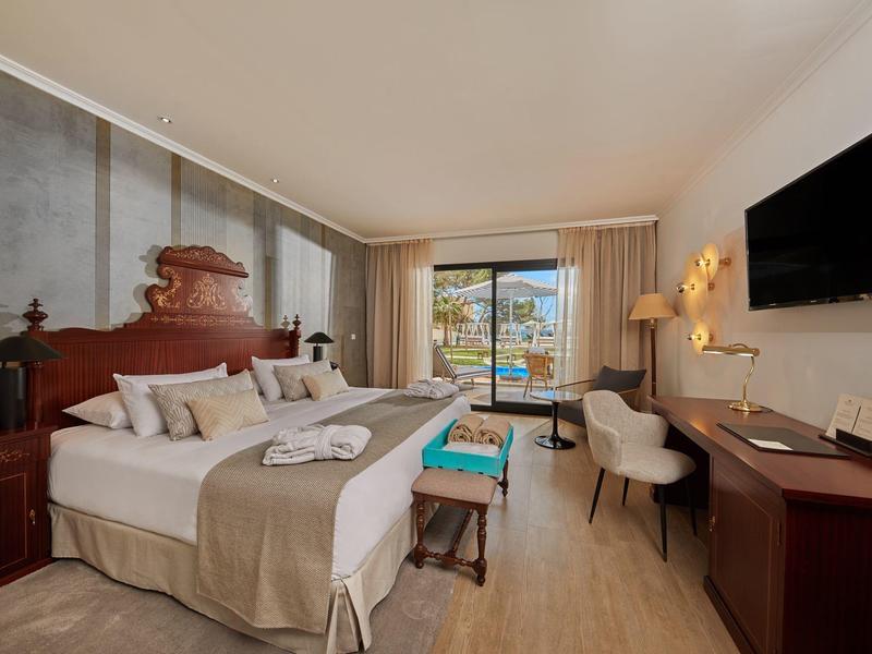 Chambre d'hôtel moderne avec lit double, bureau, chaise, télévision et balcon avec sièges extérieurs.