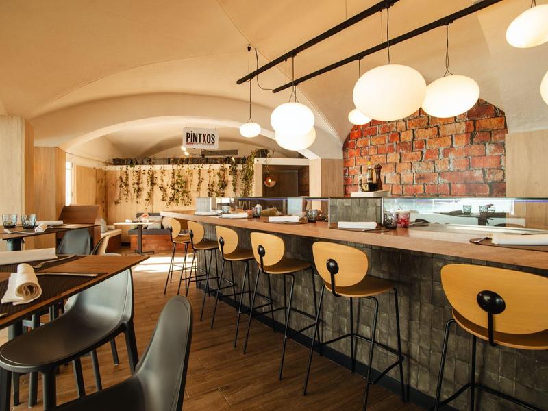 Bar moderne avec tabourets en bois, lampes suspendues et mur en briques dans un espace chaleureux.