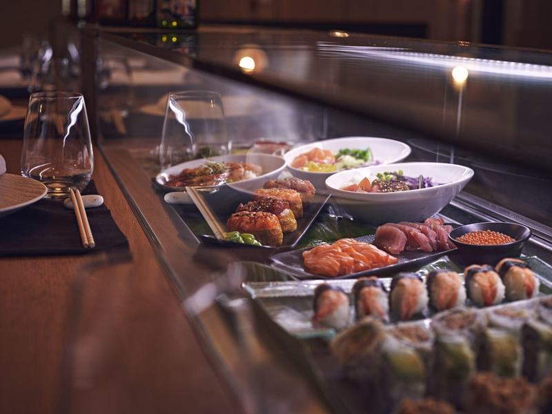 Gros plan sur diverses sushis frais et plats japonais sur un comptoir en verre dans un restaurant.
