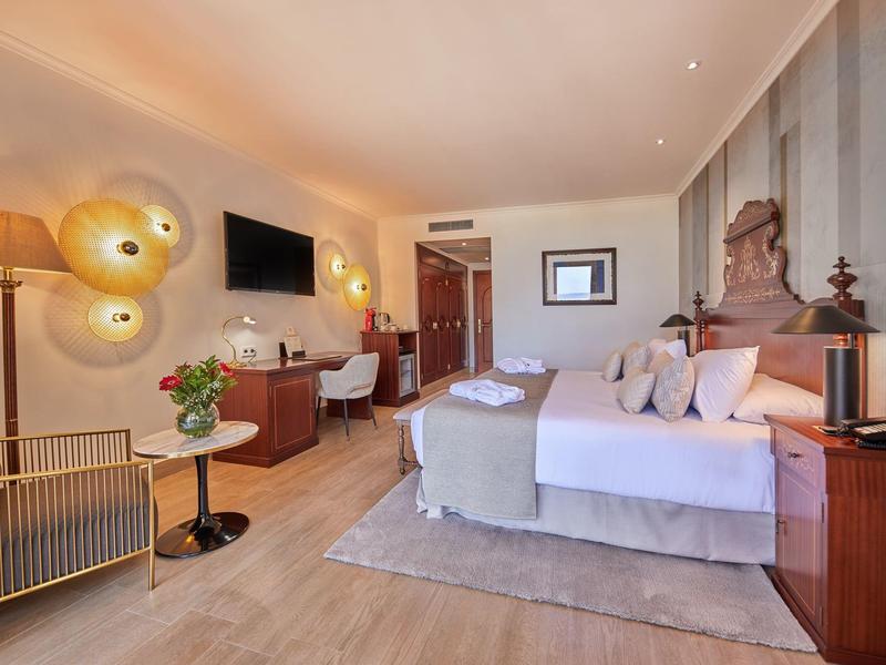 Chambre d'hôtel spacieuse avec lit, bureau, TV et lampes élégantes sous un éclairage chaud.