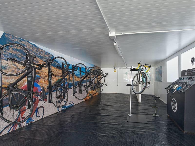 Salle de rangement moderne pour vélos avec vélos sur des supports et un stand de réparation dans un espace lumineux.