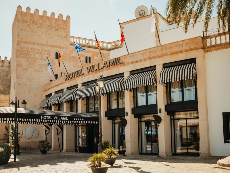 Façade de l'hôtel Villasol avec drapeaux et palmier sous un ciel ensoleillé