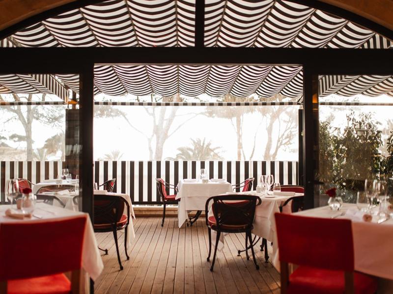 Coin repas extérieur chaleureux avec chaises rouges sous un toit en bois et mur rayé.