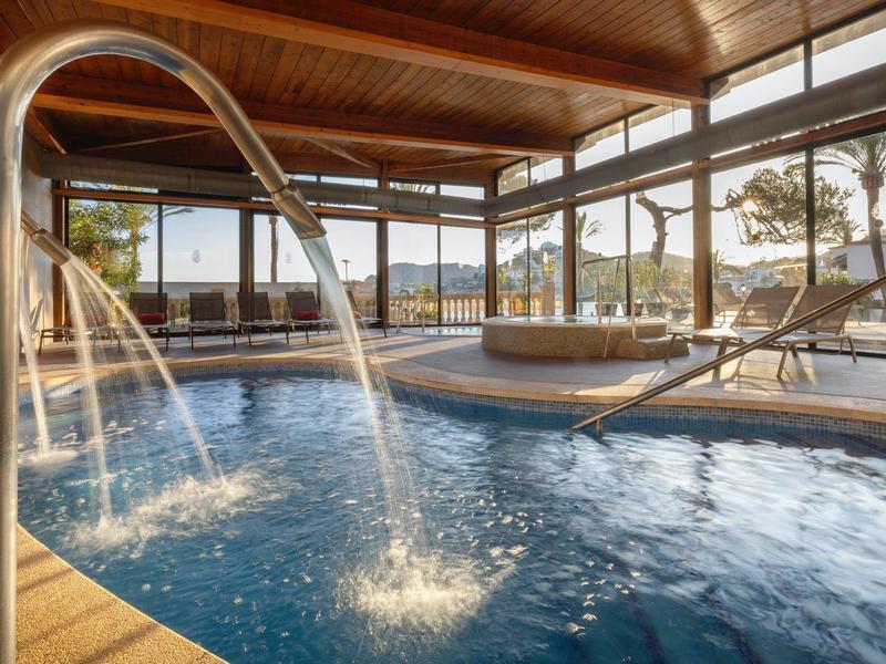 Piscine intérieure avec jets d'eau, grandes fenêtres, plafond en bois et espace de vue extérieur.