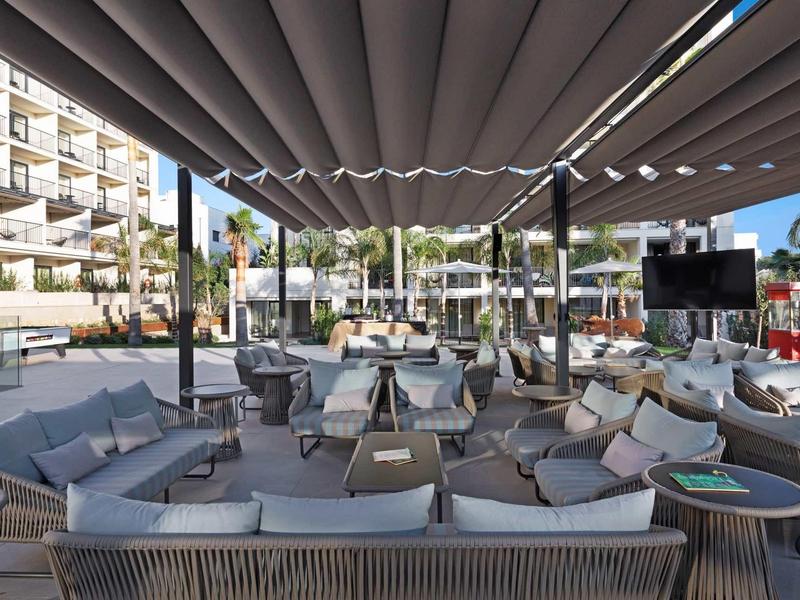 Moderní venkovní lounge s pohodlnými pohovkami a stolky pod látkovou střechou.