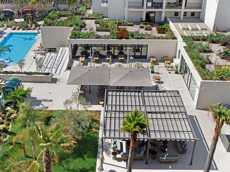 Moderní hotelový komplex s bazénem, zahradou a zastřešenými posezeními na slunci.