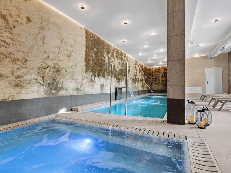 Moderní wellness s bazénem, vířivkou a lehátky v elegantním prostředí.