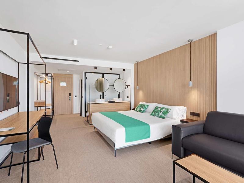 Světý hotelový pokoj s manželskou postelí, posezením a moderním pracovním koutem.