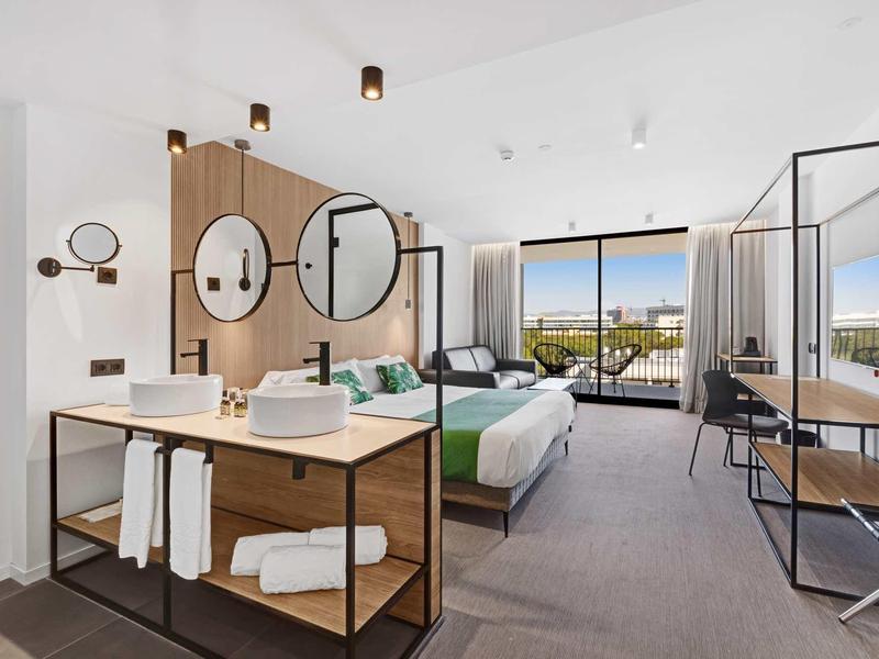 Moderní hotelový pokoj s manželskou postelí, otevřenou koupelnou a velkým oknem s výhledem.