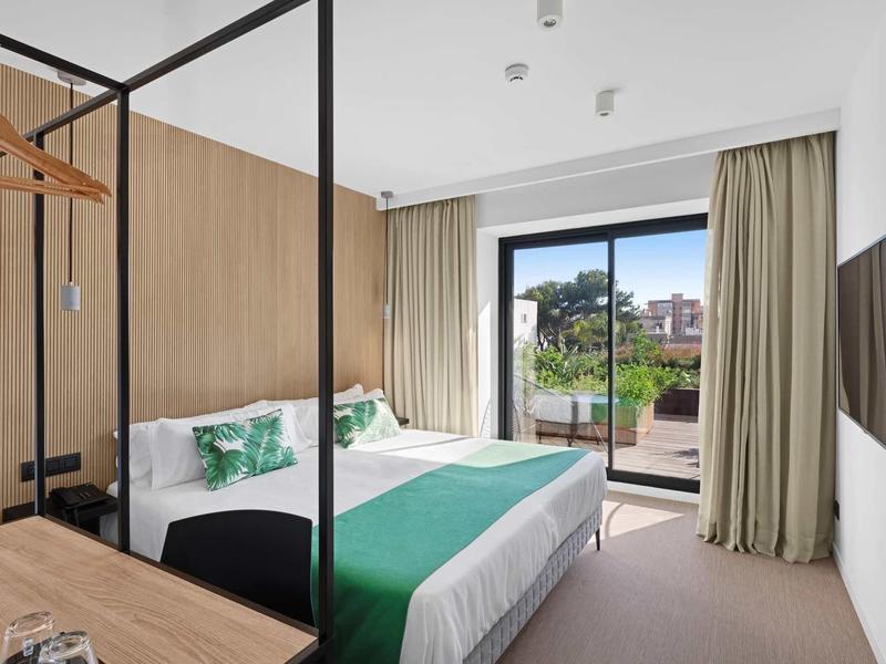 Moderní hotelový pokoj s manželskou postelí, zeleno-bílým povlečením a výhledem na terasu.