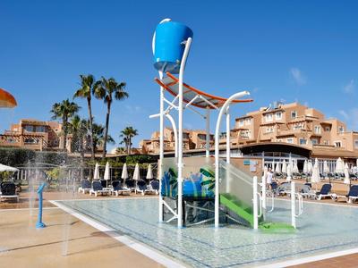 Wasserspiel mit Eimer und Rutschen in einem Poolbereich mit Liegestühlen und Palmen.