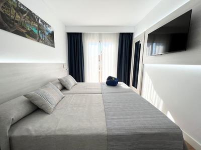 Nowoczesny pokój hotelowy z dwoma łóżkami, dużym oknem i telewizorem na ścianie.