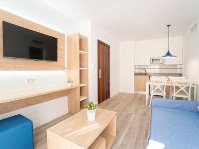 Nowoczesny salon z aneksem kuchennym, drewnianymi półkami i niebieską sofą w jasno urządzonym apartamencie wakacyjnym.