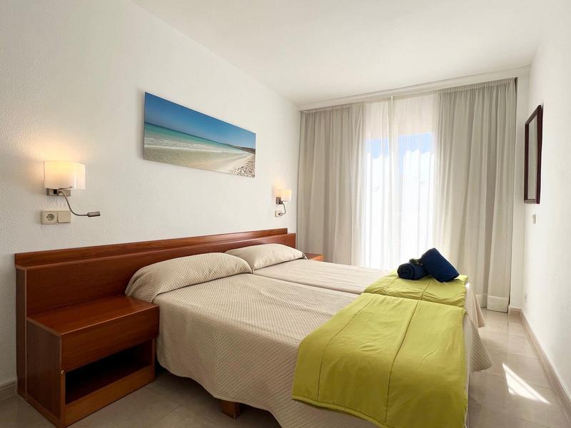 Jasny pokój hotelowy z łóżkiem podwójnym, szafką nocną, dużymi oknami i zielonym narzutem.