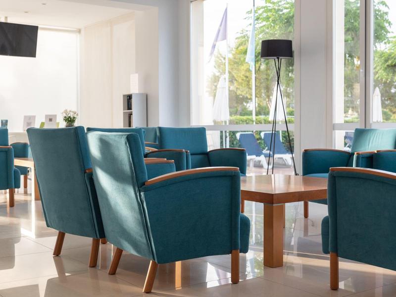 Jasne, nowoczesne lobby hotelowe z niebieskimi fotelami i drewnianymi stolikami przy dużych oknach.
