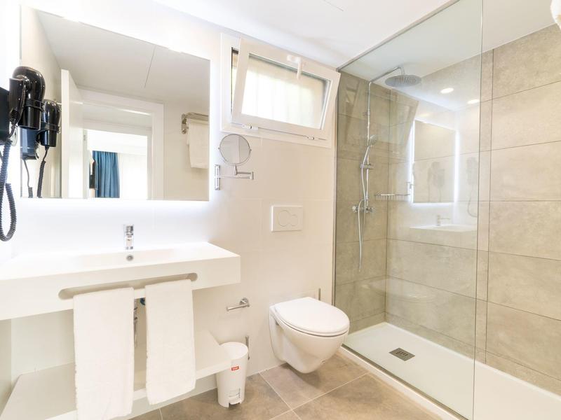 Jasna łazienka z dużym szklanym prysznicem, białą umywalką i toaletą.